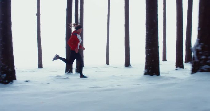 WIDE TRACKING SIDE VIEW Adult fit Caucasian female jogging on winter forest trail. 4K UHD 60 FPS SLO MO