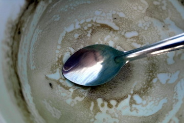 Close up of a finished cup of coffee with remains of the drink, and a dirty tea spoon