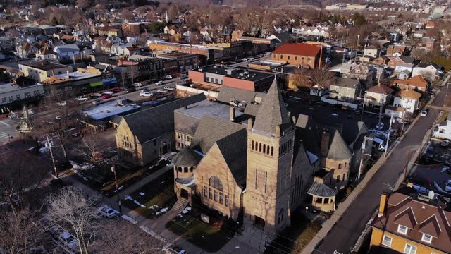 A slow push high angle forward aerial establishing shot of a church in a typical Western Pennsylvania small town business district. Pittsburgh suburbs.	 	