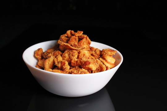 Greaves crunchy cracklings fried pork lard crust on black reflective studio background. Isolated black shiny mirror mirrored background for every concept.