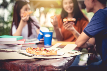 Three Asian people enjoy eating pizza at outdoors after tutoring class. Education and party concept. Food and Drinks theme. Happiness lifestyle theme.