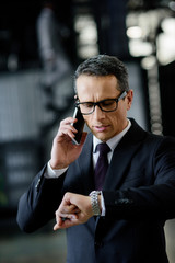 portrait of businessman checking time while talking on smartphone
