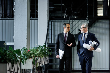businessmen with notepad and blueprints having conversation in office