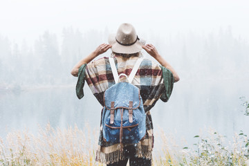 Fototapeta premium Travel woman feeling happy among amazing mountains, enjoy the nature landsape. Forest and lake, wearing backpack, hat and poncho, boho and wanderlust style