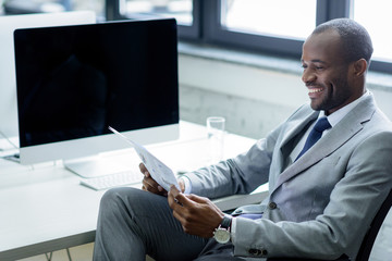 smiling african american businessman reading newspaper at workplace