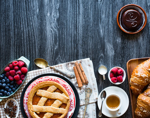 Top view of a wood table full of cakes, fruits, coffee, biscuits, spices and more