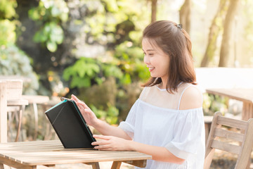 Portrait of Attractive young Asian woman wearing white casual smiling and laughing while using a tablet to chatting with her friends. Technology, Internet, and Social media concept.