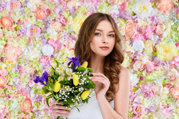 beautiful young woman with curly hair holding floral bouquet
