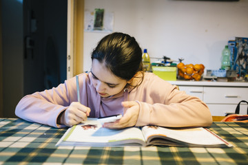 teenager does her homework in the home kitchen on the table helping herself with the smartphone