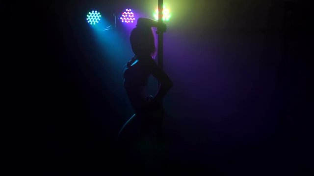 Young hot woman in sexy lingerie performs sensual pole dance, slow motion. Silhouette of a girl on the pole in a smoke-filled room.