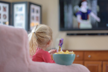 Little girl eating popcorn while watching a classic movie on TV 