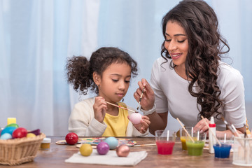Obraz na płótnie Canvas happy african american mother and daughter painting easter eggs