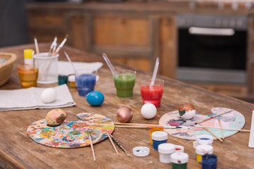 painted chicken eggs with paints and brushes on wooden table, easter concept