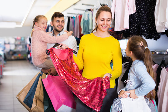 Young mother helping to daughter choosing new dress in shop
