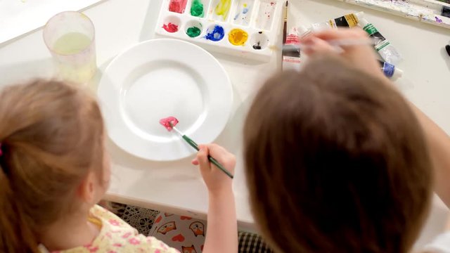 Happy family, mother and little daughter paint with paint on white plates
