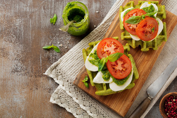 Sandwiches on green wafer with spinach and mozzarella cheese, pesto sauce, tomatoes and basil on a gray concrete old background. Selective focus. Top view.
