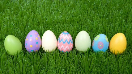 Colorful decorative and plain easter eggs lined up in a row in green grass.
