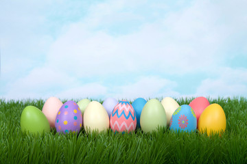 Fototapeta na wymiar Colorful decorative and plain easter eggs lined up in a row in green grass. Blue sky with clouds in background.
