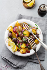 Warm potato salad with olives, pepper, parsley and red onion on old white ceramic plate on gray concrete background. Selective focus. Top view. Copy space.