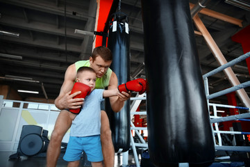 Little boy training with coach and punchbag in boxing gym