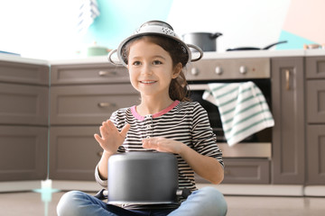 Cute little girl playing with saucepan as drum indoors