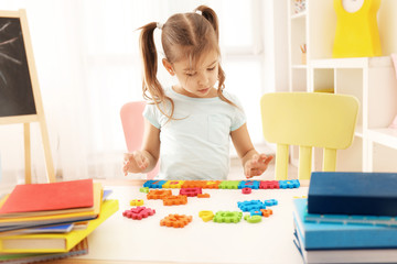 Cute little girl playing with figures while doing homework indoors