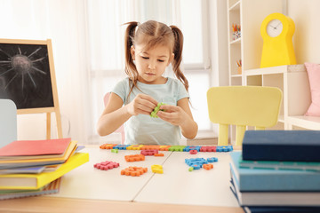 Cute little girl playing with figures while doing homework indoors