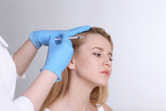 Young woman with hair problem receiving injection on light background