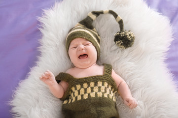 Cute little baby in elf costume lying on fur, top view