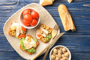 Plate with tasty chicken bruschettas and ingredients on wooden table