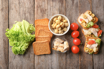 Tasty chicken bruschettas and ingredients on wooden table, flat lay