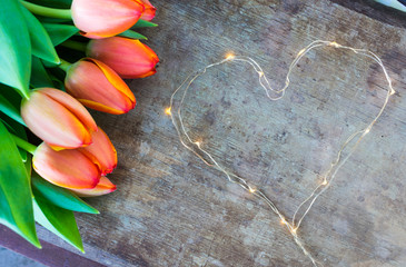 View of colorful orange tulips and led lights chain shaped in heart form on old rustic vintage...