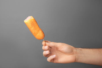 Woman holding tasty corn dog on gray background