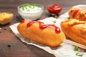 Tasty corn dogs with sauces on wooden table