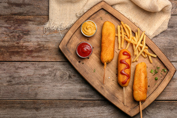 Tasty corn dogs with sauces on wooden tray