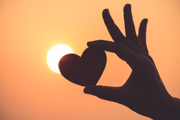 Close up and Silhouette of hand holding red heart during sunset background. Happy, Love, Valentine's day idea, sign, symbol, concept.