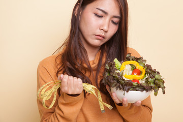 Unhappy Asian woman with measuring tape and salad.