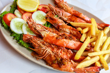 Plate grilled spicy prawn shrimps kebabs, vegetables, french fries with sauces and greens on light background.