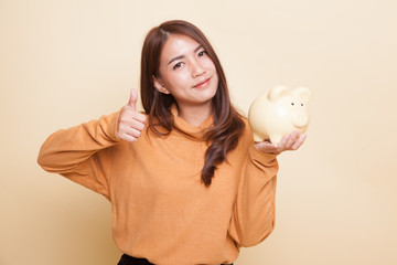 Asian woman thumbs up with pig coin bank.