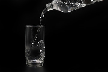 Wasser wird aus Plastikflasche in Glas gegossen auf schwarzen Hintergrund
