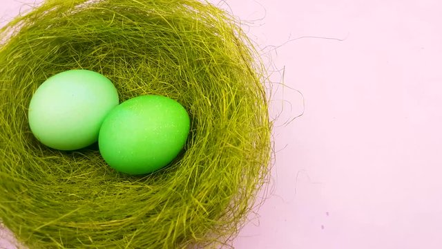 Color easter eggs in nice nest on pastel pink background.