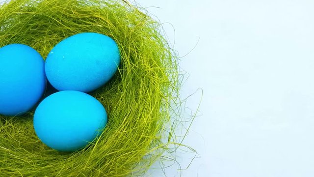Easter color eggs in nest on pastel blue background. 
