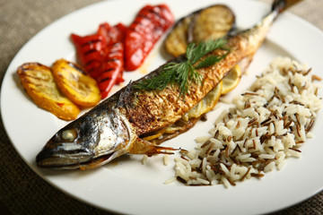 Healthy and proper food, grilled fish and vegetables with lemon and black and white rice on a white plate. Against the background of sacking and a wooden table. Low-calorie food