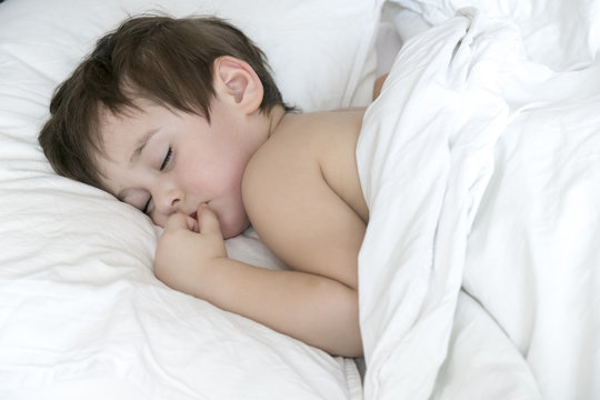 Peaceful baby lying on a bed while sleeping in a bright room. cute two year old Asian boy on white the pillow