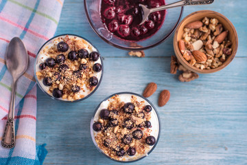 yogurt parfait with jam, nuts and berries in a glass on a rustic wooden background - top view