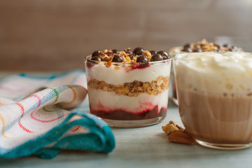 A cup of coffee with whipped cream and parfait for breakfast on a rustic wooden background close-up