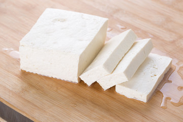 Tofu piece and cubes on chopping board.  Closeup.