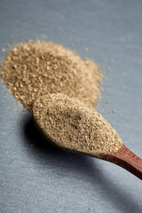 Closeup black pepper whole in wooden spoon on black stone table