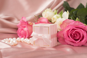 A bouquet of fresh roses and a gift on a background of a gentle satin. Copy space.Holiday concept.