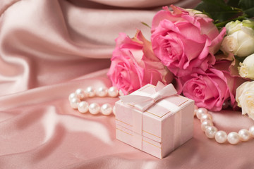 A bouquet of fresh roses and a gift on a background of a gentle satin. Copy space.Holiday concept.